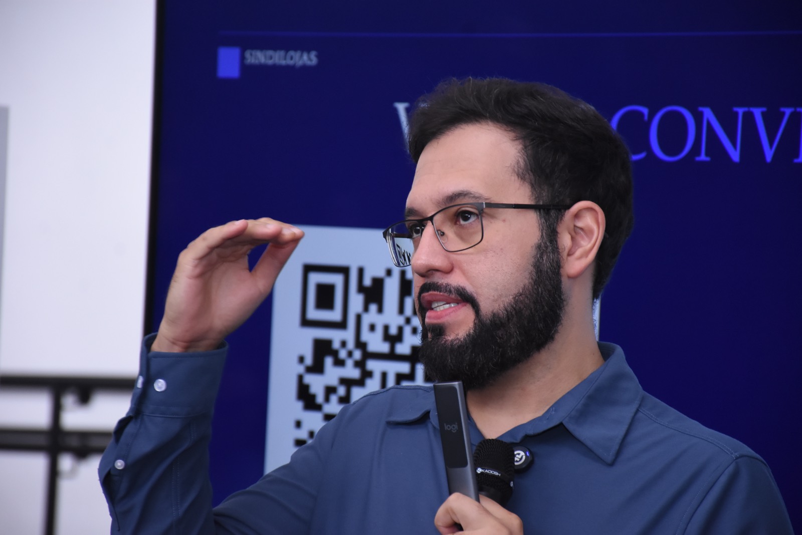 Calebe Salvia, de óculos e camisa azul, explica um ponto da palestra segurando o microfone